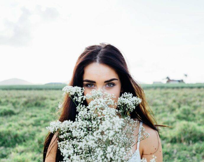 Woman standing in a field, holding a bouquet of baby's breath in front of her face so that only her eyes are showing